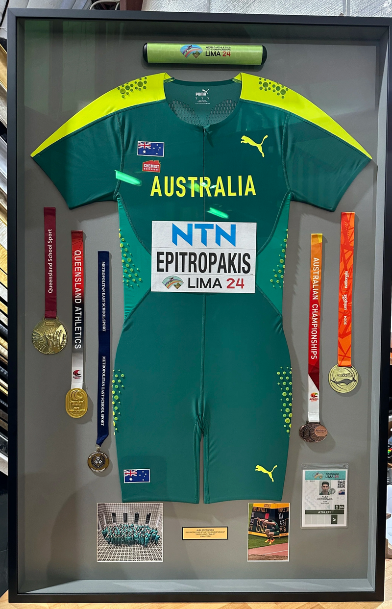 Green Australian sports jersey with yellow accents displayed in a frame, surrounded by medals and certificates.